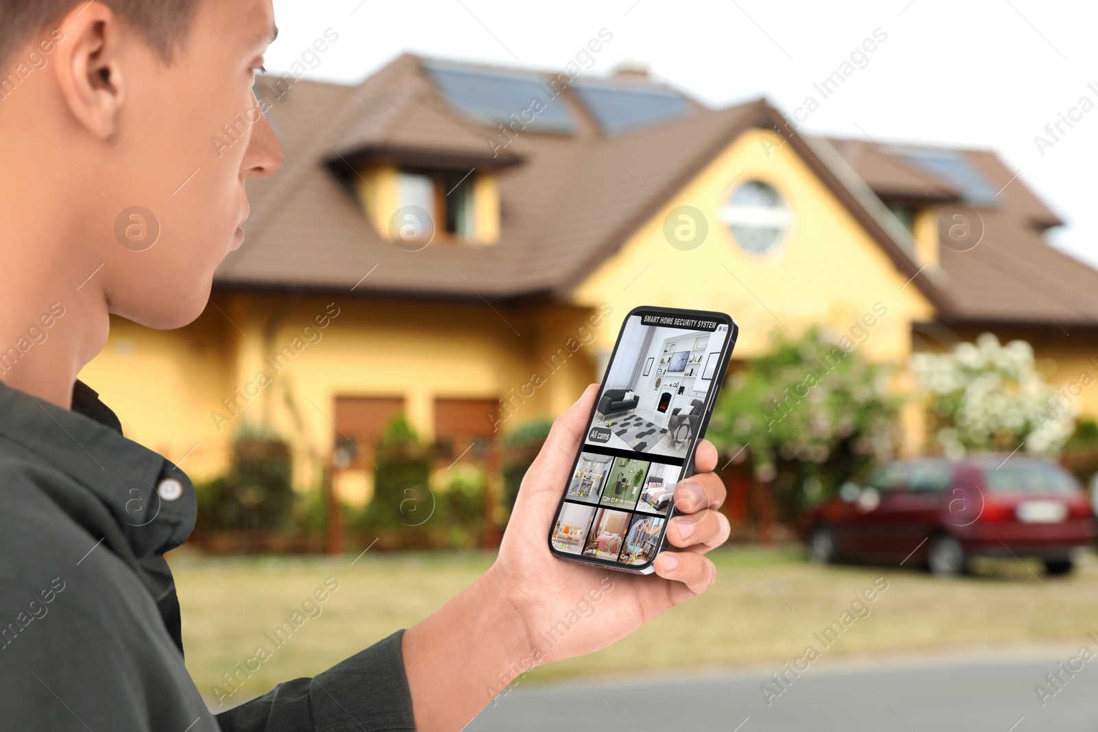 Image of Man using smart home security system on smartphone near house outdoors. Device showing different rooms through cameras