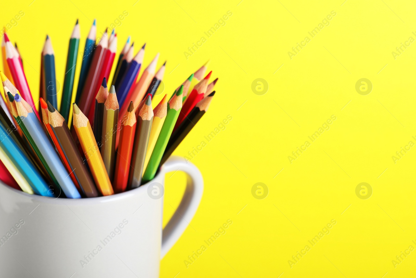 Photo of Colorful pencils in light cup on yellow background, closeup. Space for text