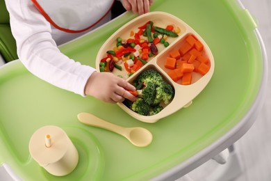 Photo of Little baby eating healthy food in high chair, closeup. Above view