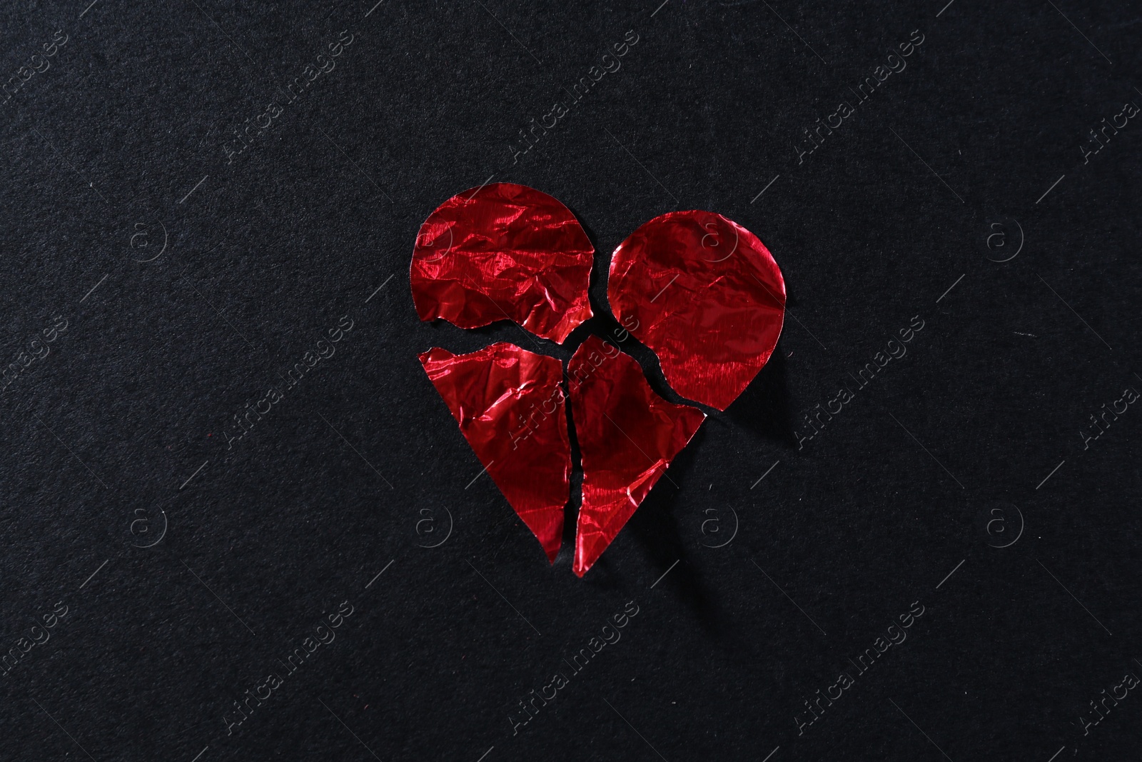 Photo of Red crumpled paper heart broken to pieces on black background, top view. Breakup concept