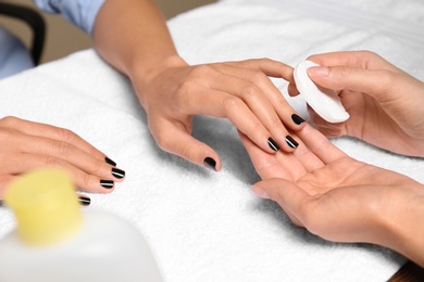 Manicurist removing polish from client's nails in salon, closeup