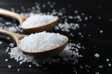 Photo of Organic salt in spoons on black wooden table, closeup. Space for text