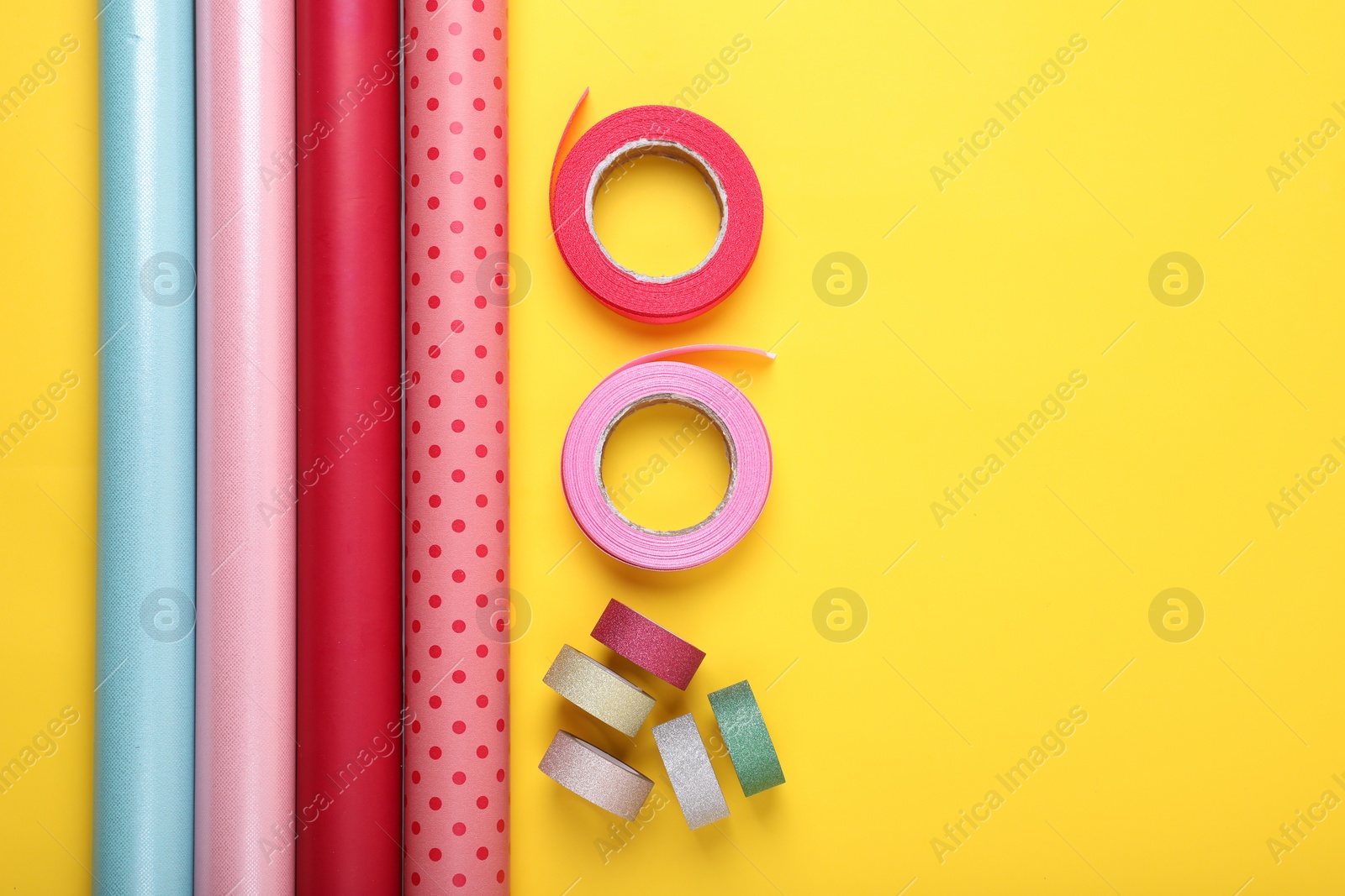 Photo of Rolls of colorful wrapping papers and ribbons on yellow background, flat lay. Space for text