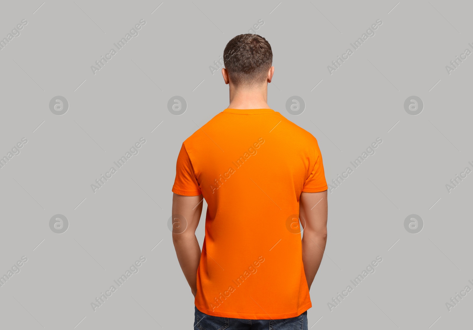 Photo of Man wearing orange t-shirt on light grey background, back view. Mockup for design