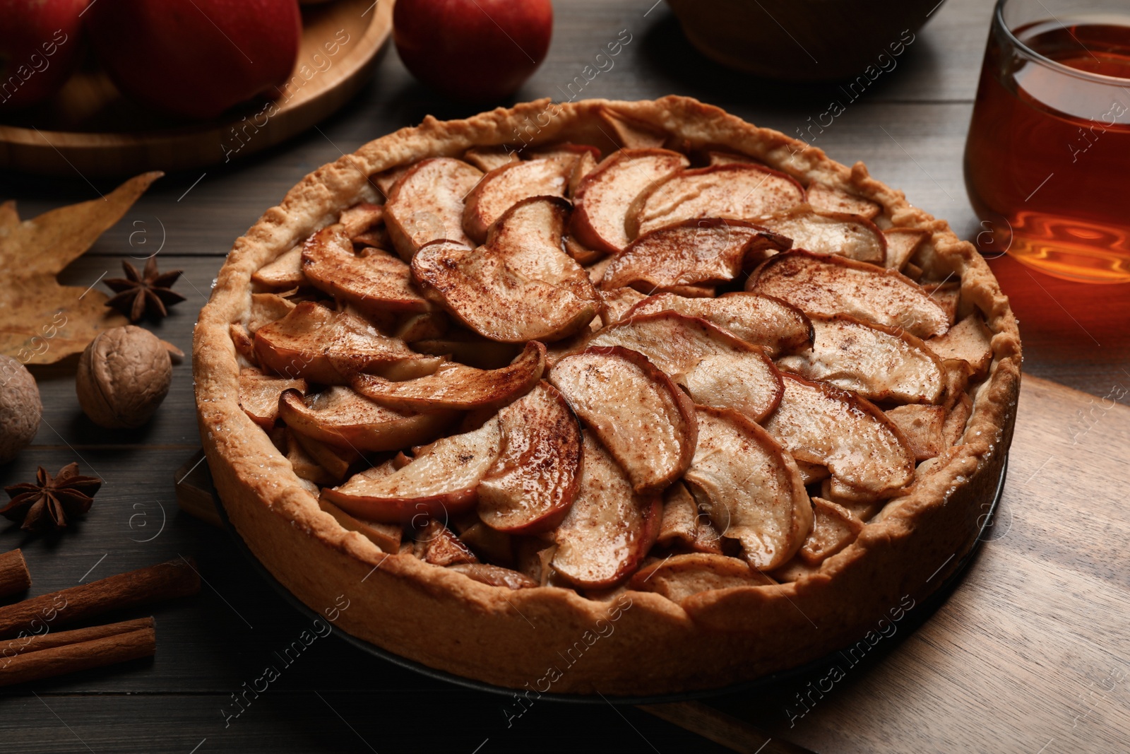 Photo of Delicious apple pie, ingredients and cup of tea on wooden table