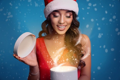 Image of Beautiful woman in Santa hat opening Christmas gift on blue background