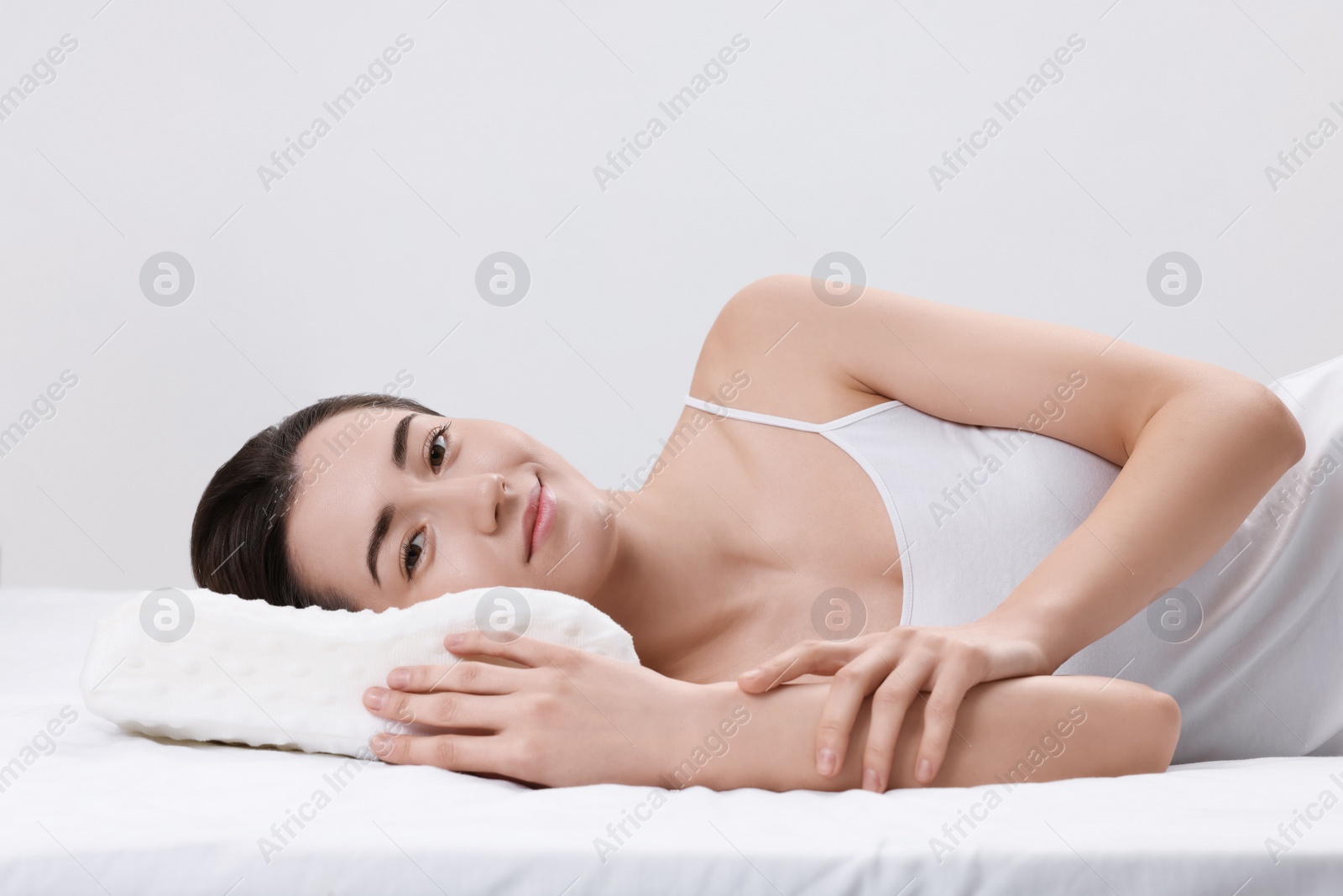 Photo of Woman lying on orthopedic pillow against light grey background