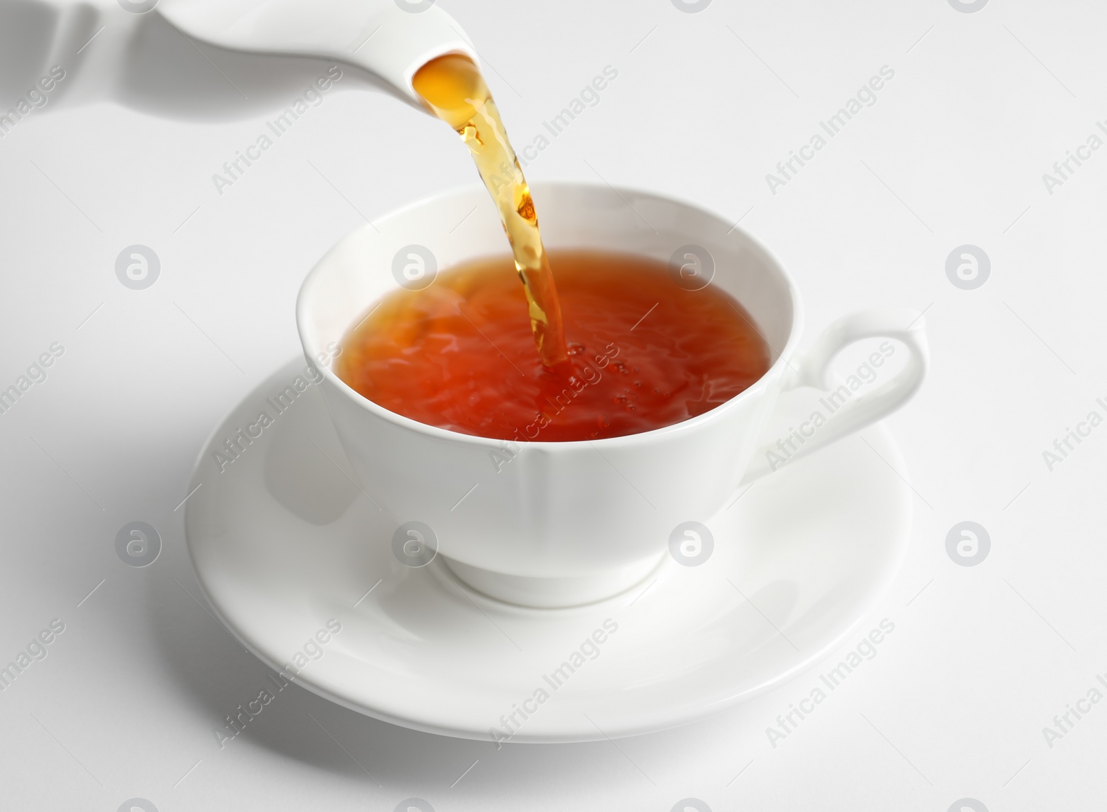 Photo of Pouring hot tea into porcelain cup on white background