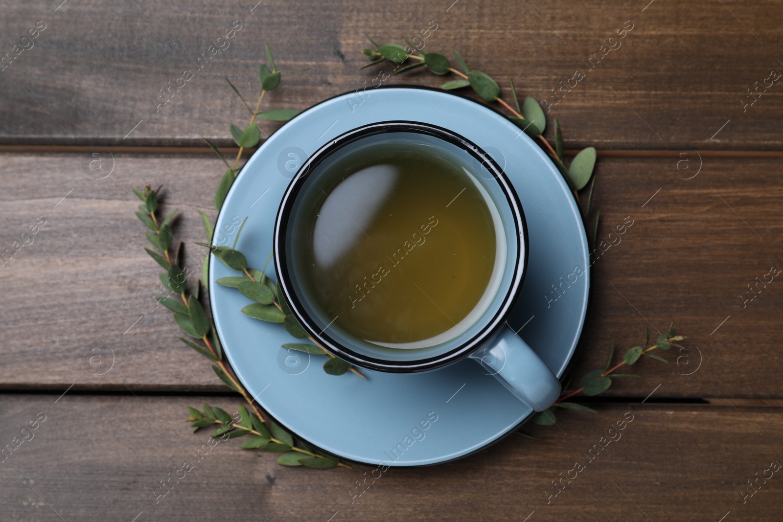 Photo of Cup of green tea and eucalyptus leaves on wooden table, flat lay