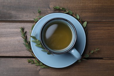 Photo of Cup of green tea and eucalyptus leaves on wooden table, flat lay