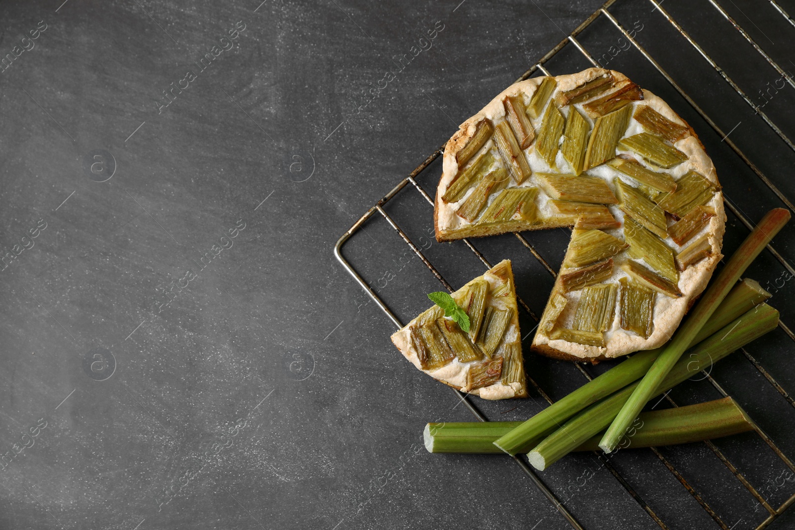 Photo of Freshly baked rhubarb pie and stalks on black table, flat lay. Space for text