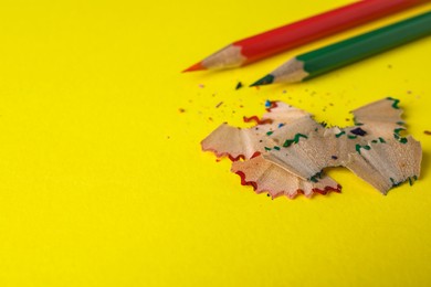 Photo of Color pencils and shavings on yellow background, closeup. Space for text