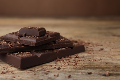 Photo of Pieces and shavings of tasty chocolate on wooden table, closeup. Space for text