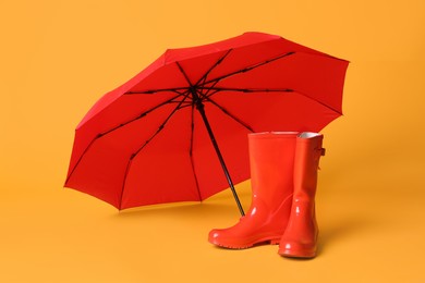 Photo of Open red umbrella and rubber boots on yellow background