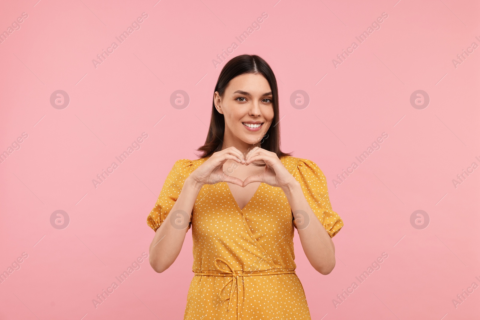 Photo of Young woman making heart with hands on pink background