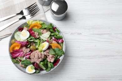 Photo of Bowl of delicious salad with canned tuna and vegetables served on white wooden table, flat lay. Space for text