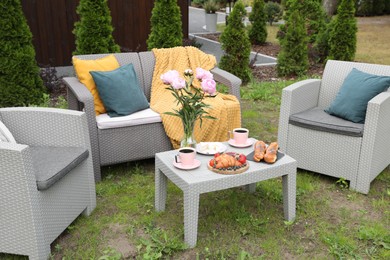 Photo of Breakfast served outdoors. Morning drink, food and vase with flowers on rattan table