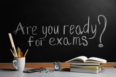 Different stationery and alarm clock on light table near blackboard with phrase Are You Ready For Exams