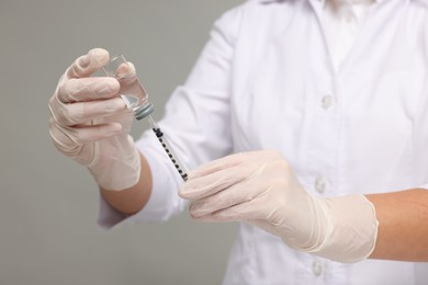 Doctor filling syringe with medication from glass vial on grey background, closeup