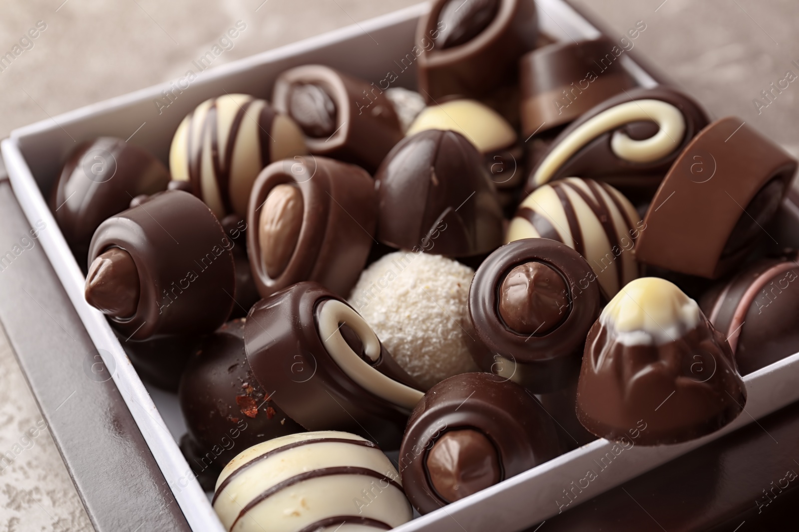 Photo of Box with different tasty chocolate candies on table, closeup