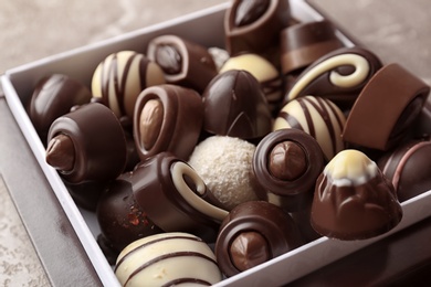 Photo of Box with different tasty chocolate candies on table, closeup