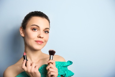 Young woman with lipstick and makeup brush on color background. Professional cosmetic products