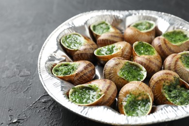 Photo of Delicious cooked snails on dark textured table, closeup