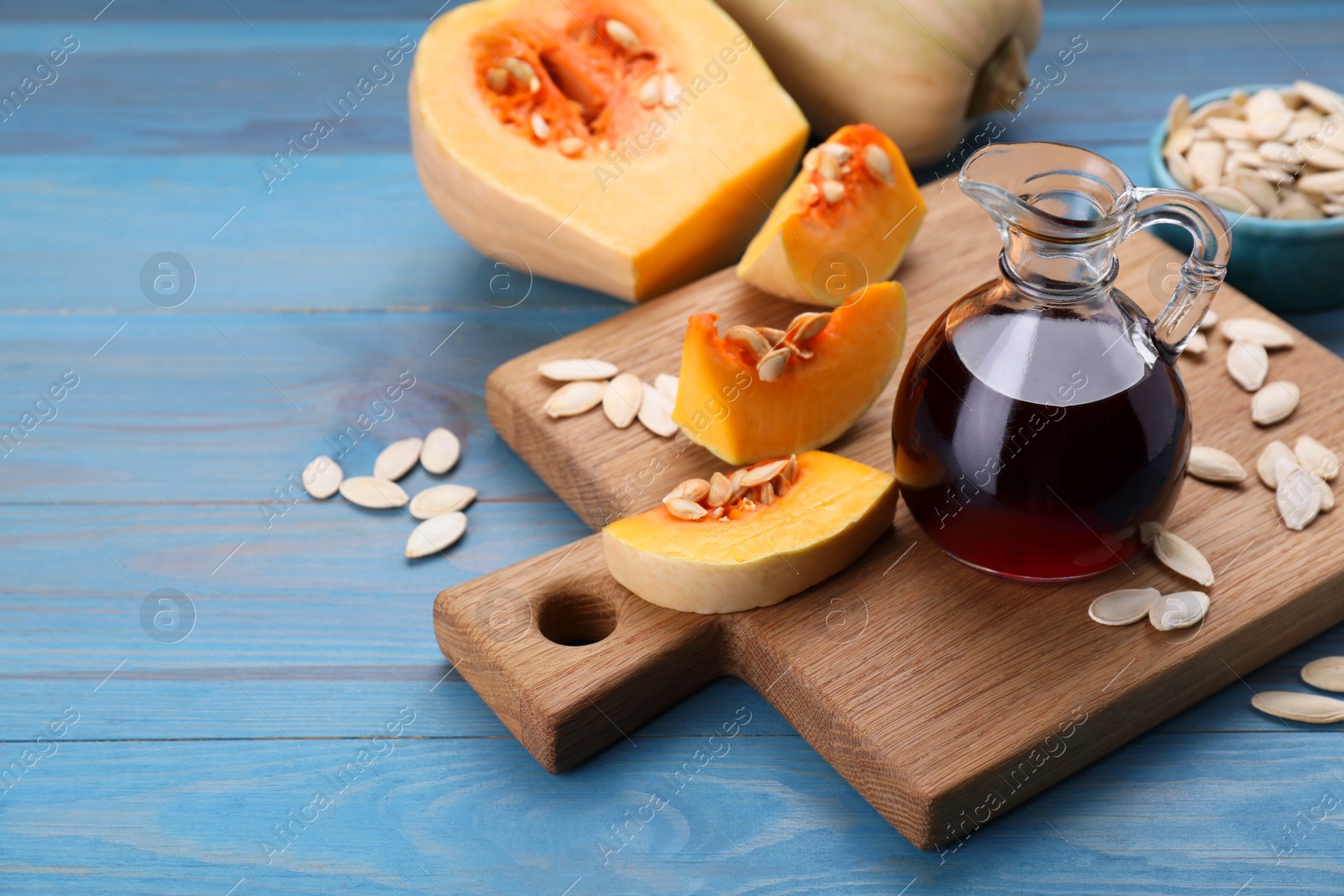 Photo of Fresh pumpkin seed oil in glass jug on blue wooden table. Space for text