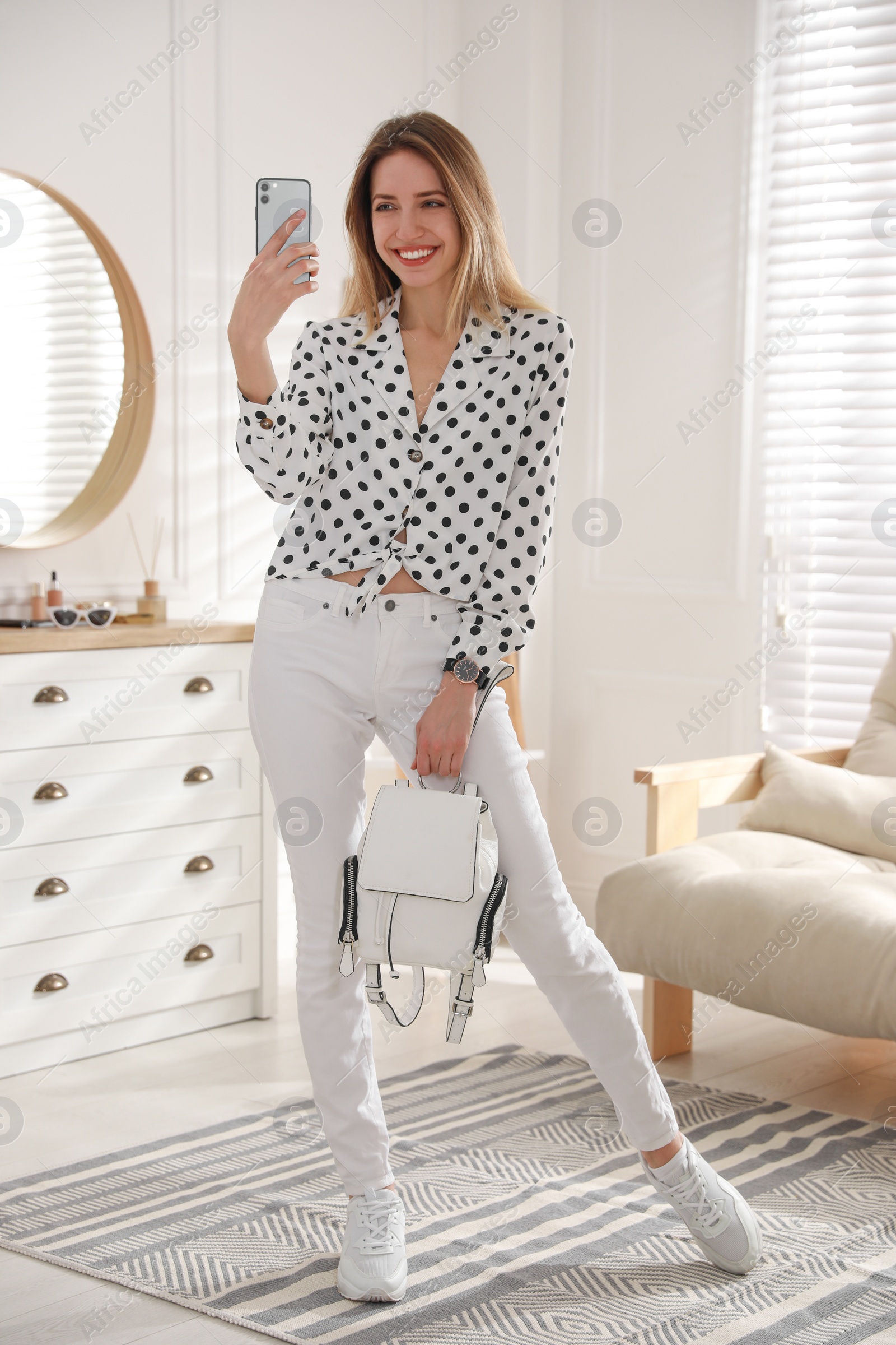 Photo of Young woman taking mirror selfie in stylish outfit at home. Morning routine