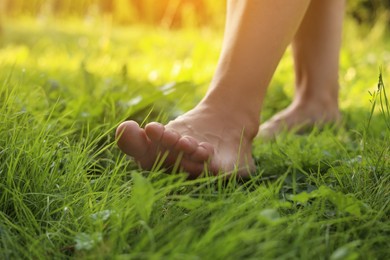 Photo of Woman walking barefoot on green grass, closeup