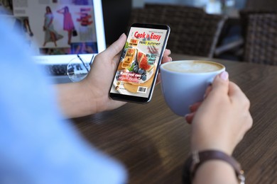 Photo of Woman reading online magazine on mobile phone in cafe, closeup