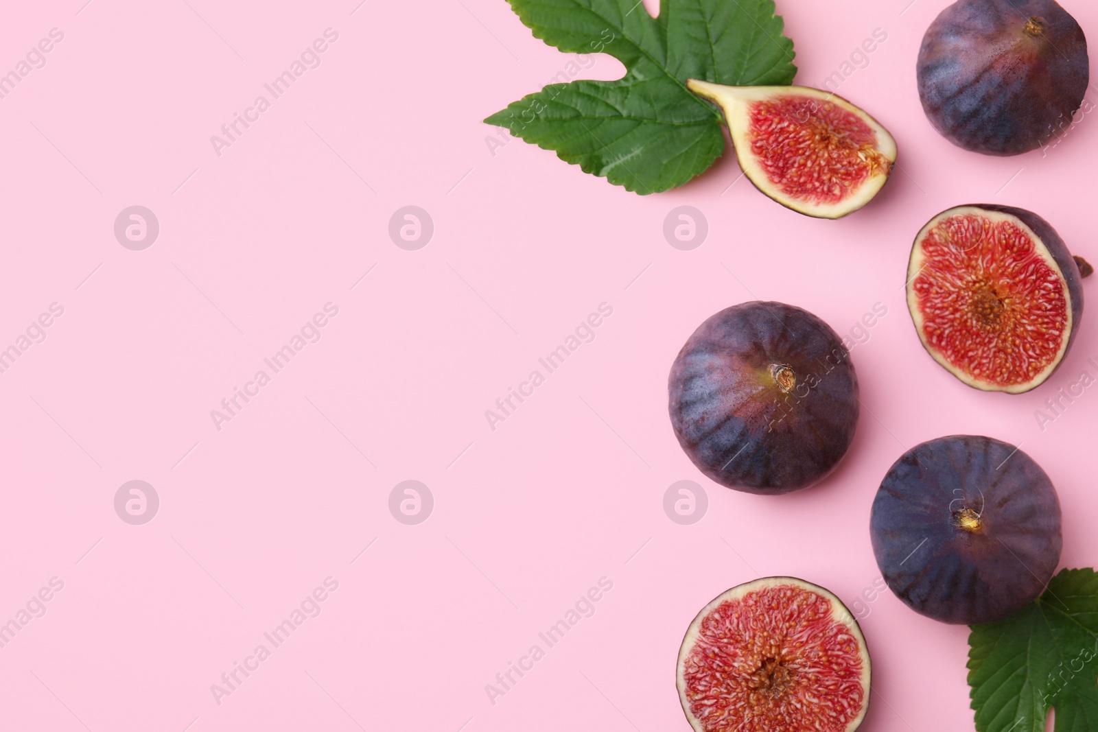 Photo of Fresh ripe figs with green leaves on pink background, flat lay. Space for text