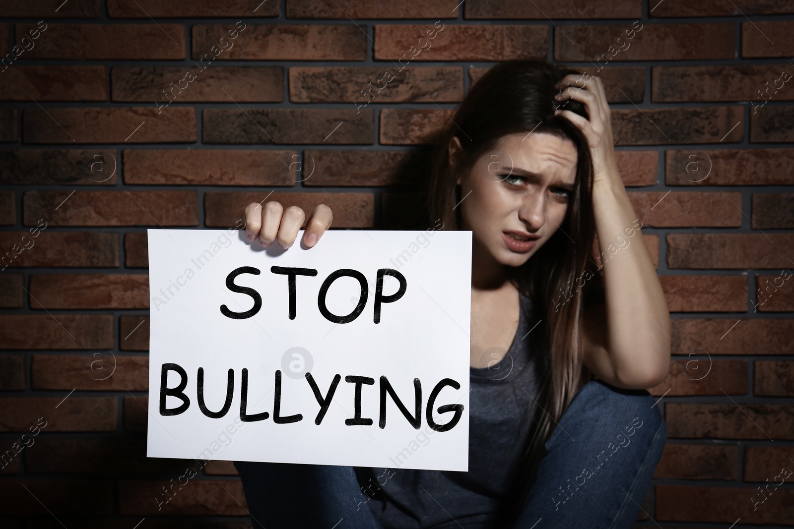Image of Abused teen girl with sign STOP BULLYING near brick wall
