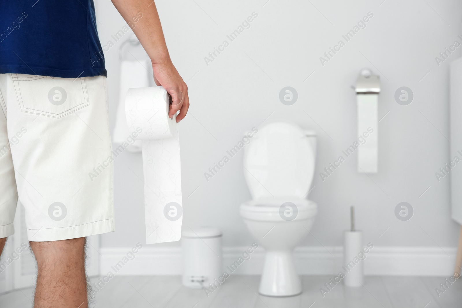Photo of Young man with bath tissue standing near toilet bowl at home
