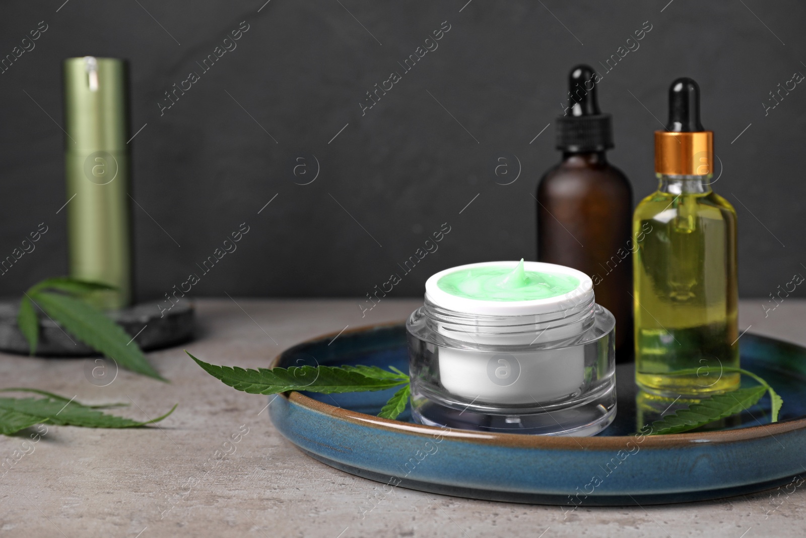 Photo of Hemp cosmetics and green leaves on light grey table