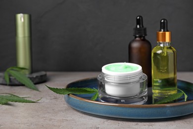 Hemp cosmetics and green leaves on light grey table