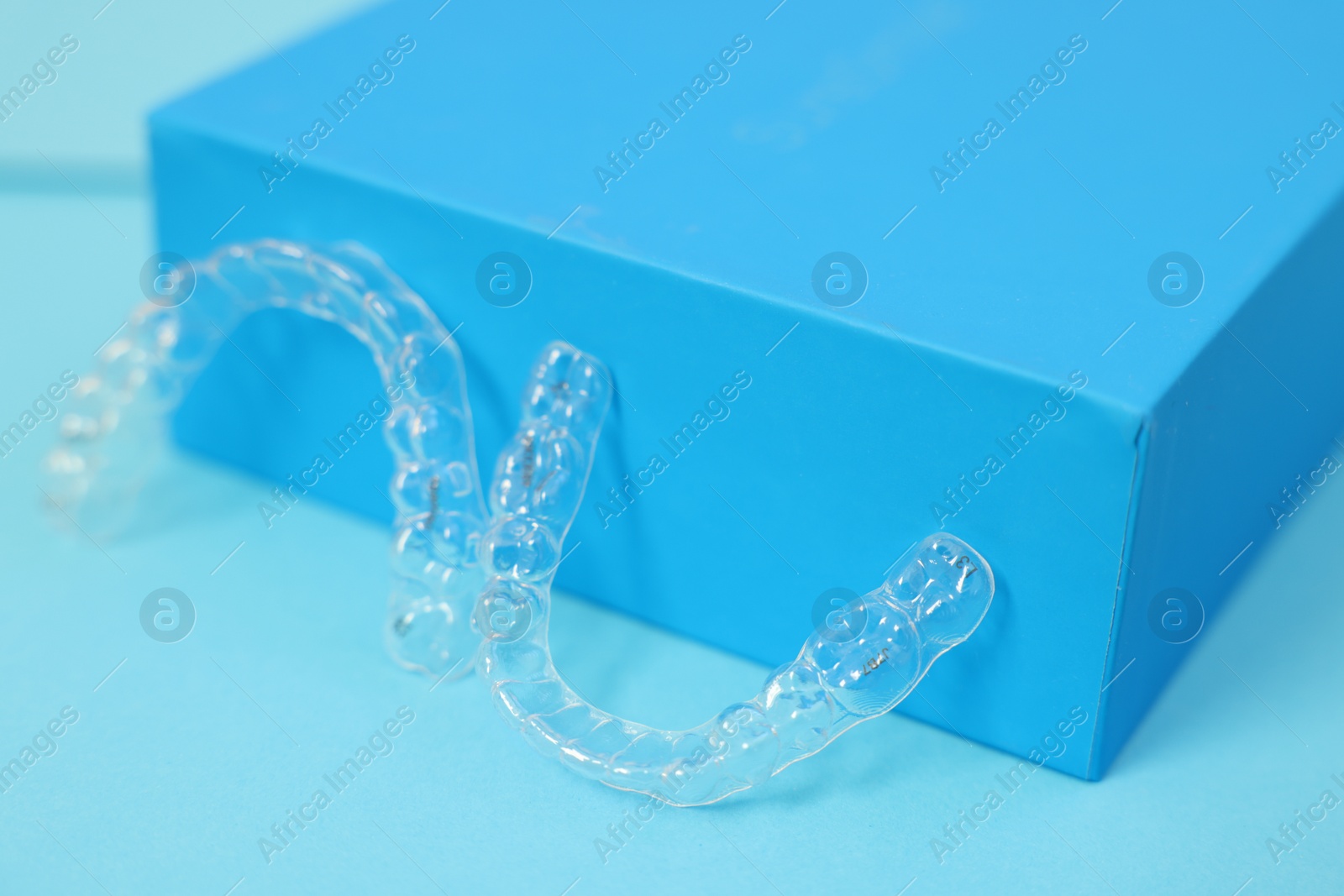 Photo of Transparent dental aligners on light blue background, closeup