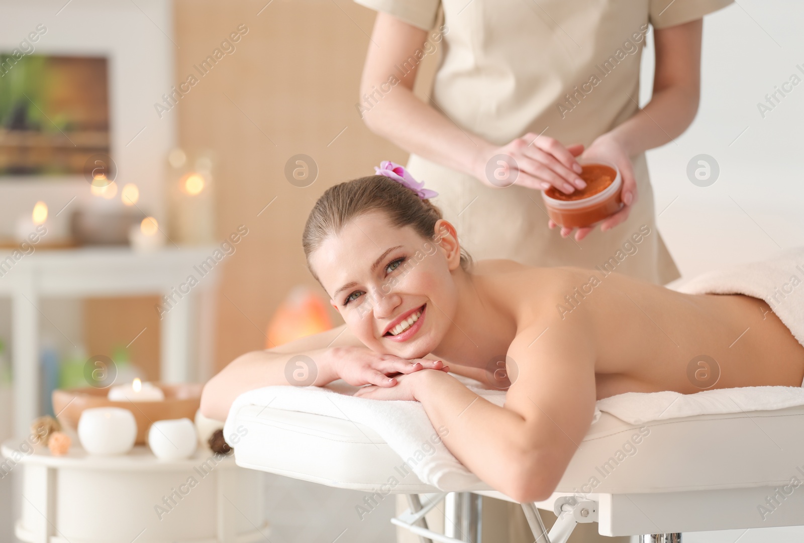 Photo of Beautiful young woman having massage with body scrub in spa salon