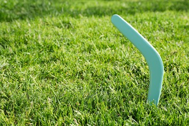 Photo of Turquoise wooden boomerang in green grass outdoors, space for text