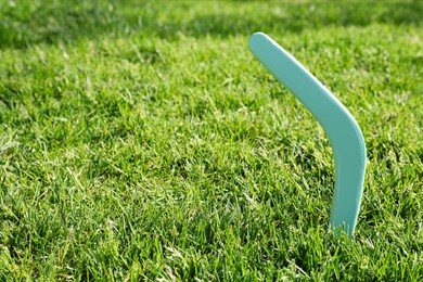 Turquoise wooden boomerang in green grass outdoors, space for text