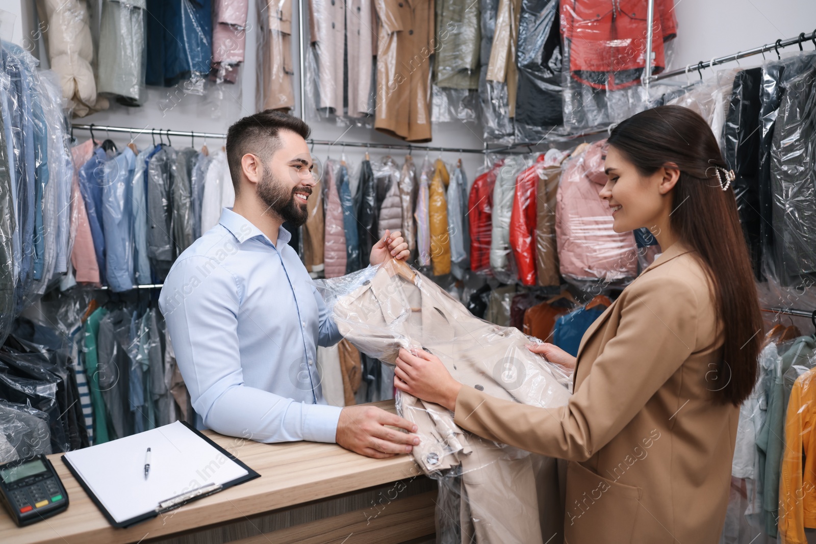 Photo of Dry-cleaning service. Happy worker giving coat to client indoors