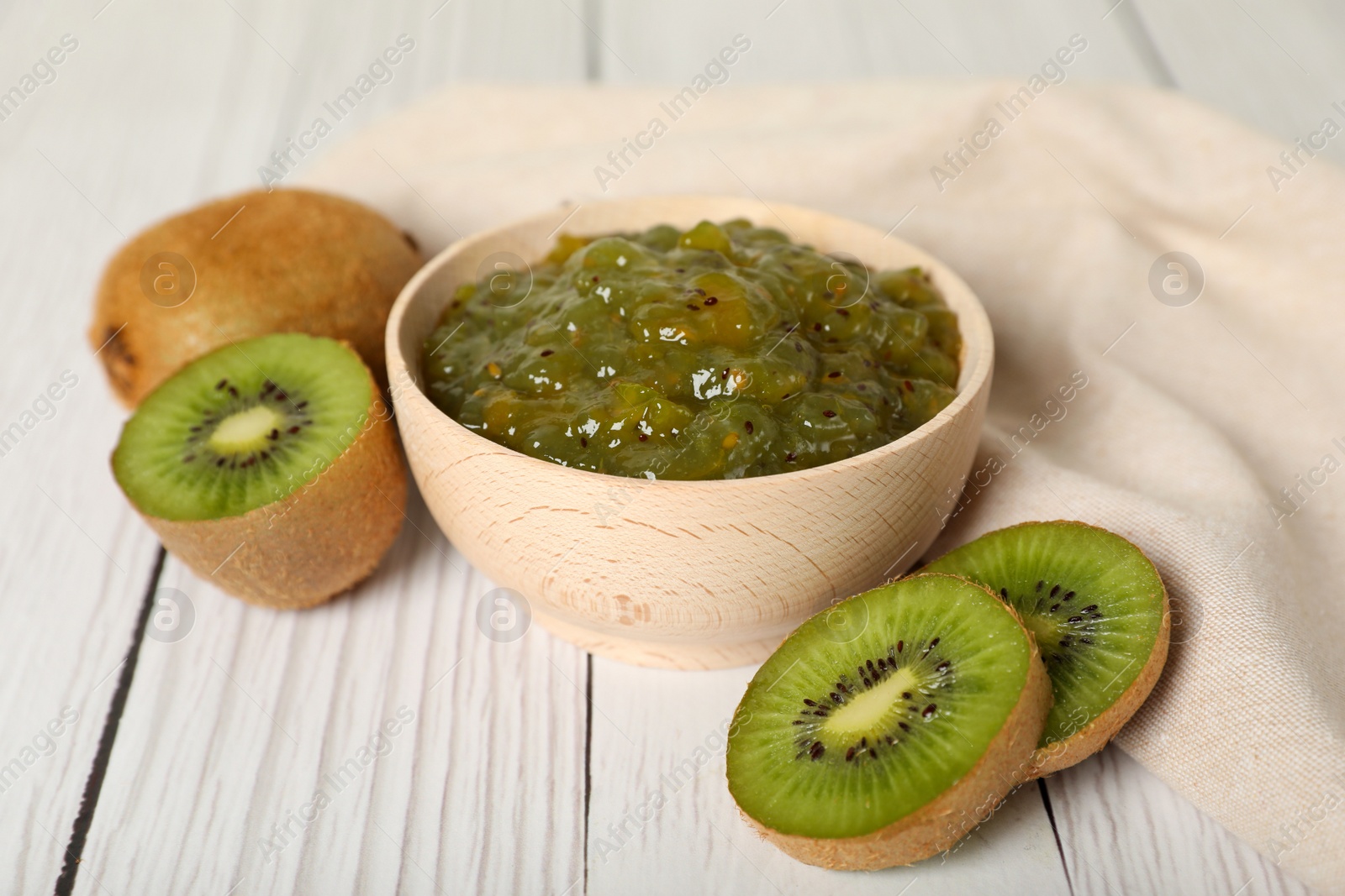 Photo of Bowl of delicious kiwi jam and fresh fruits on white wooden table