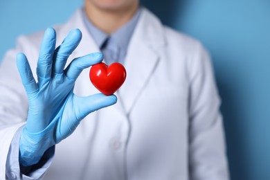 Doctor wearing medical gloves holding decorative heart on light blue background, closeup