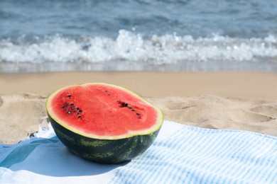 Photo of Half of fresh juicy watermelon on beach blanket near sea, space for text