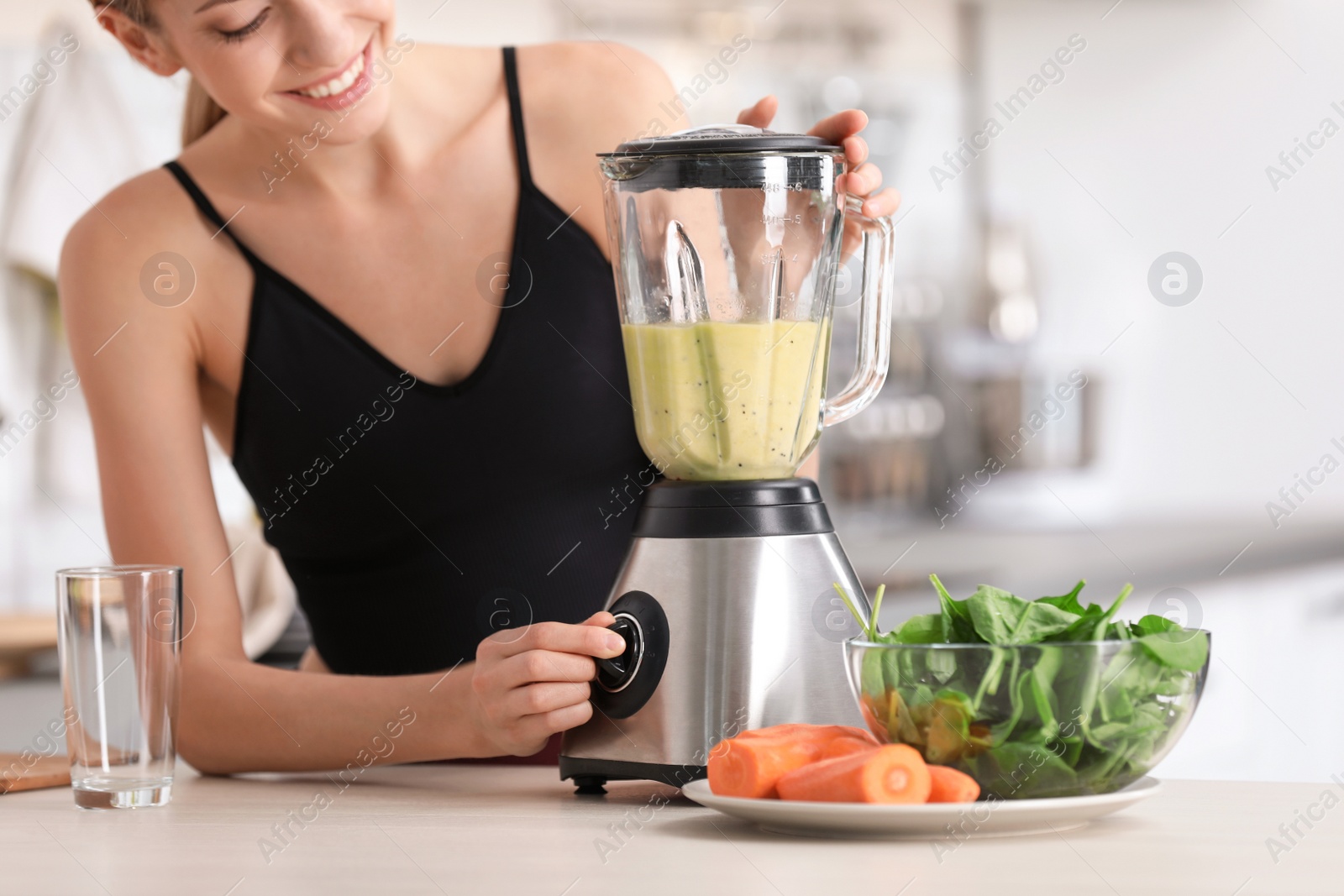 Photo of Young woman preparing tasty healthy smoothie at table in kitchen