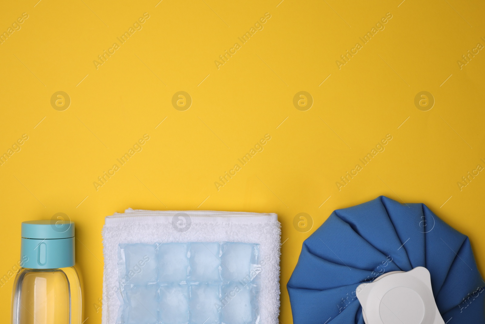 Photo of Bottle of water, ice pack, cold compress and towel on yellow background, flat lay with space for text. Heat stroke treatment