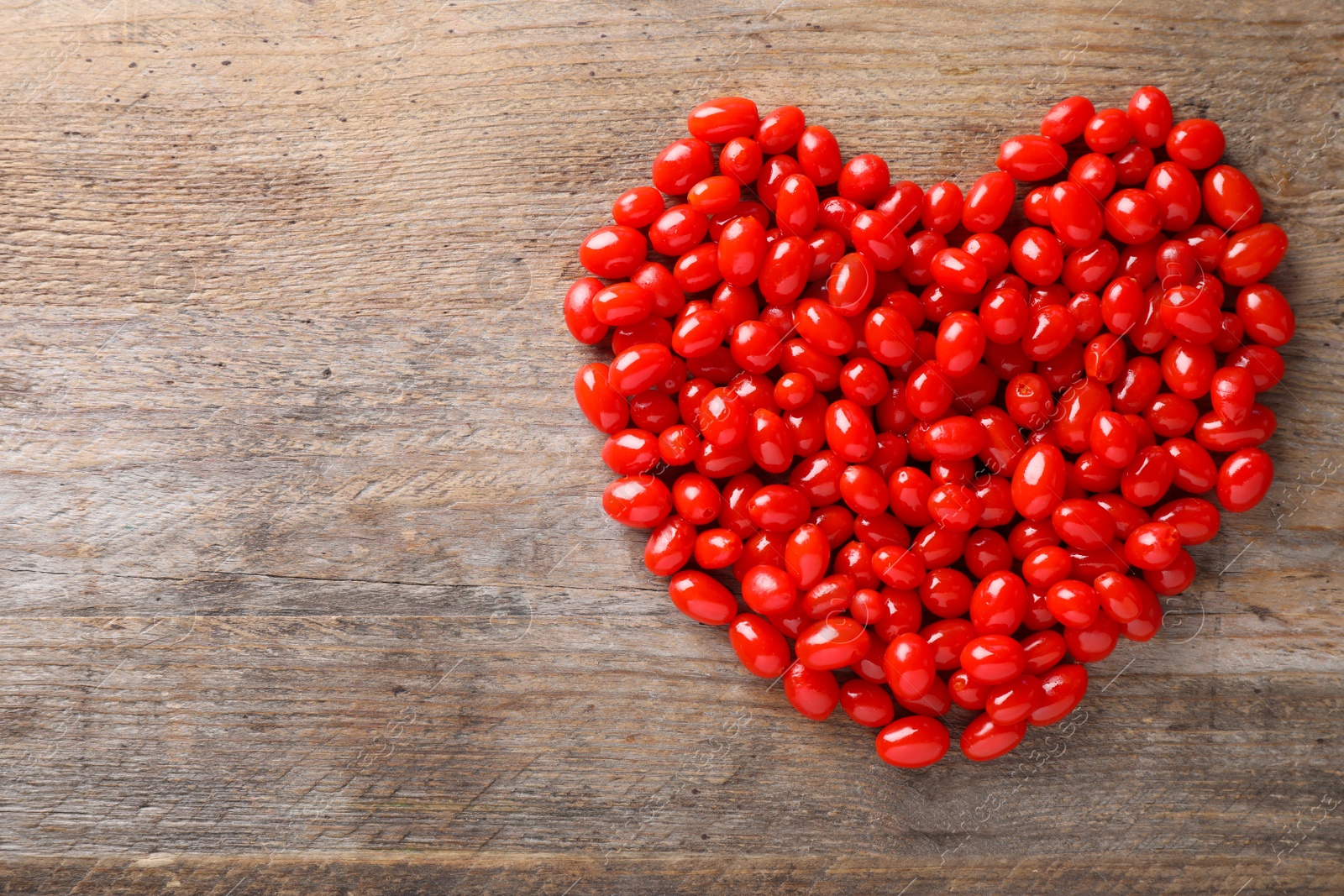 Photo of Heart shaped pile of fresh ripe goji berries on wooden table, top view. Space for text