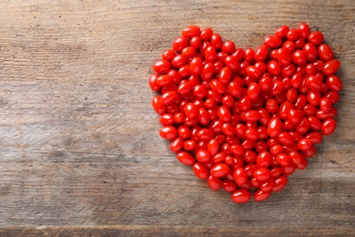 Heart shaped pile of fresh ripe goji berries on wooden table, top view. Space for text