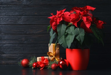 Pot with poinsettia (traditional Christmas flower) and gift boxes on table against wooden background. Space for text