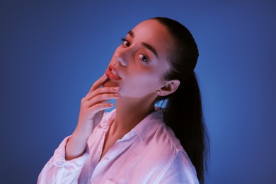 Portrait of beautiful young woman posing on blue background with neon lights